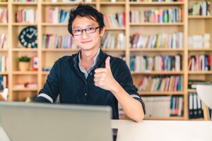 Asian man with laptop, thumbs up, at home office, library